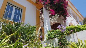 Un bâtiment à la façade jaune, doté de grandes fenêtres et d’un balcon orné de fleurs roses.