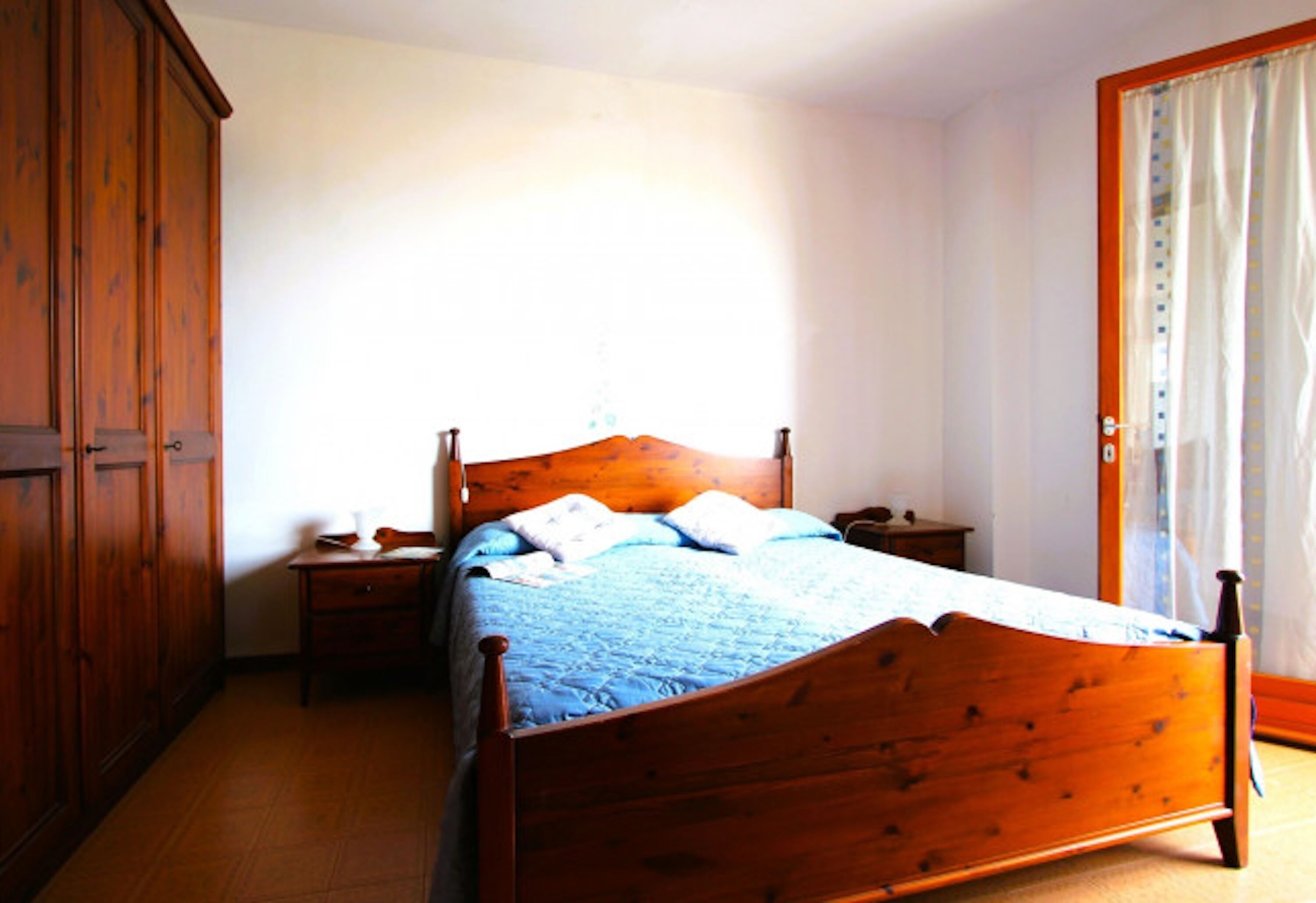 Un dormitorio con cama de madera, mesita de noche, armario y ventana con cortinas.