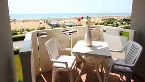 A balcony with a table and two chairs, overlooking a beach and resort area. - Amazing beachfront apartment-Beahost (Bibione)