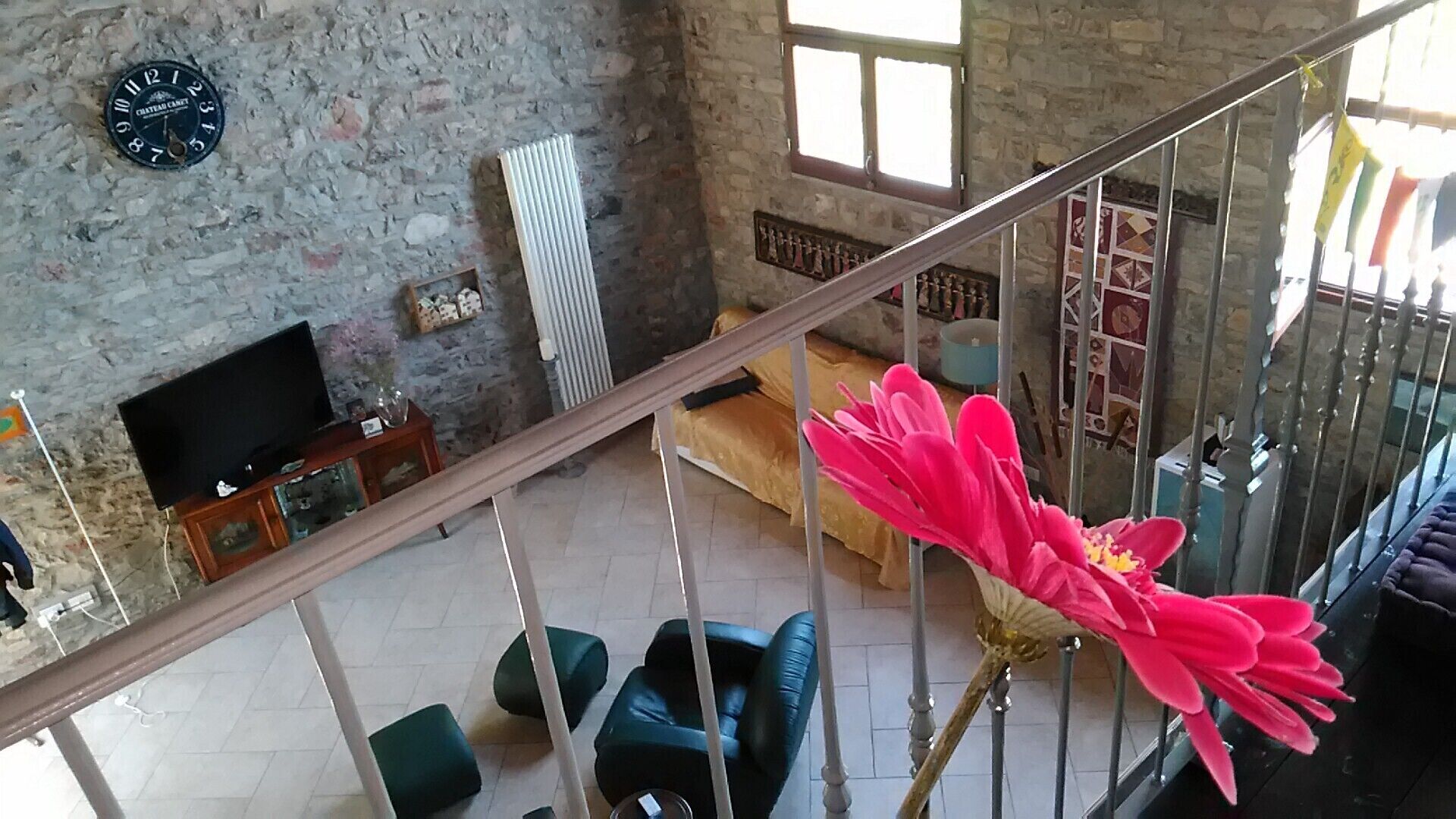 Een kamer met hoge plafonds, een stenen muur, een televisie, een radiator en een grote roze bloem op de voorgrond.