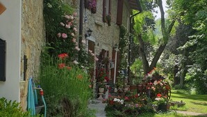 Un bâtiment en pierre avec un chemin de jardin menant à une porte, une chaise bleue et des plantes en pot.
