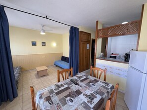Une pièce de taille modeste comprenant un lit, une petite table, un coin cuisine et un ventilateur de plafond.
