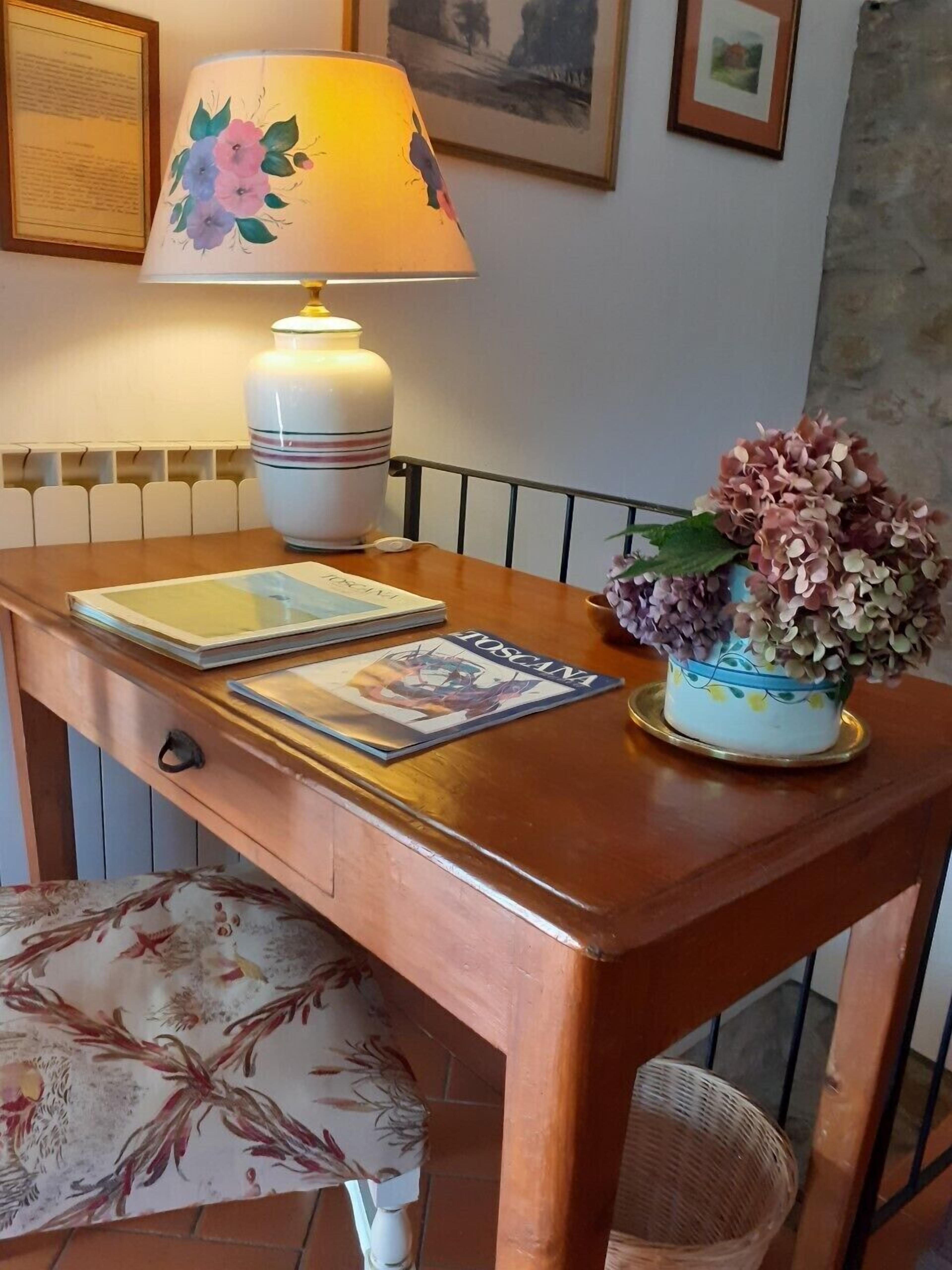 Un tavolo in legno con una lampada, un vaso con fiori e una sedia.
