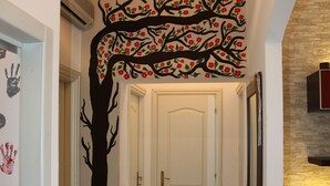 Un couloir avec une fresque représentant un arbre sur le mur, une porte blanche et un radiateur.