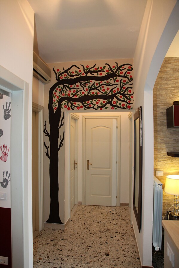 Un couloir avec une fresque représentant un arbre sur le mur, une porte blanche et un radiateur.