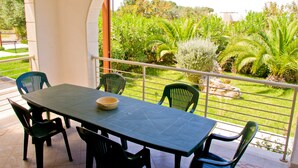 Un balcon avec une table et des chaises, donnant sur un jardin luxuriant où poussent différentes plantes et arbres.