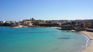 Une ville côtière dotée d’une plage de sable, d’eaux turquoise et limpides, et de bâtiments qui bordent la côte.