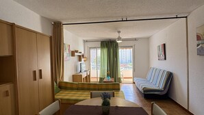 Ett kompakt bostadsutrymme med ett matbord, en soffa, en bänk och en liten köksdel.