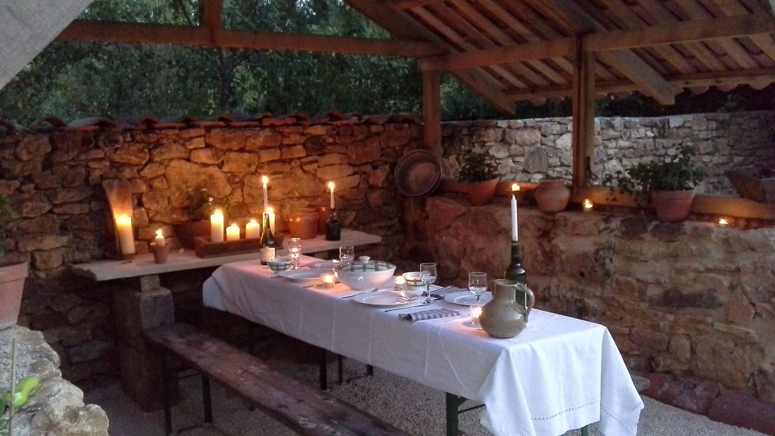 An outdoor dining area with a stone wall backdrop, wooden benches, and a table set for a meal.