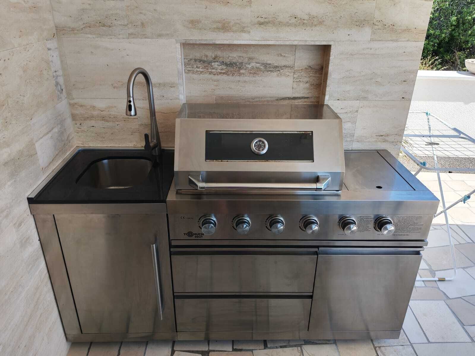 Cocina exterior de acero inoxidable con pileta, horno integrado y parrilla.