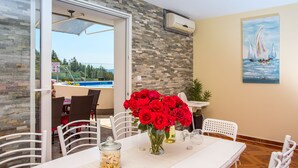 Un comedor con una mesa dispuesta para dos personas, un jarrón de rosas rojas y vistas a una piscina.