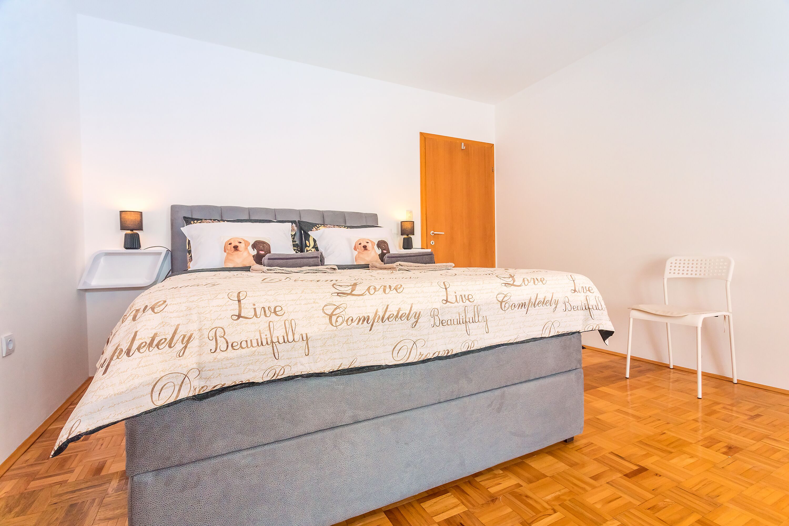 A bedroom with a bed, bedside tables, a chair, and a wooden door.