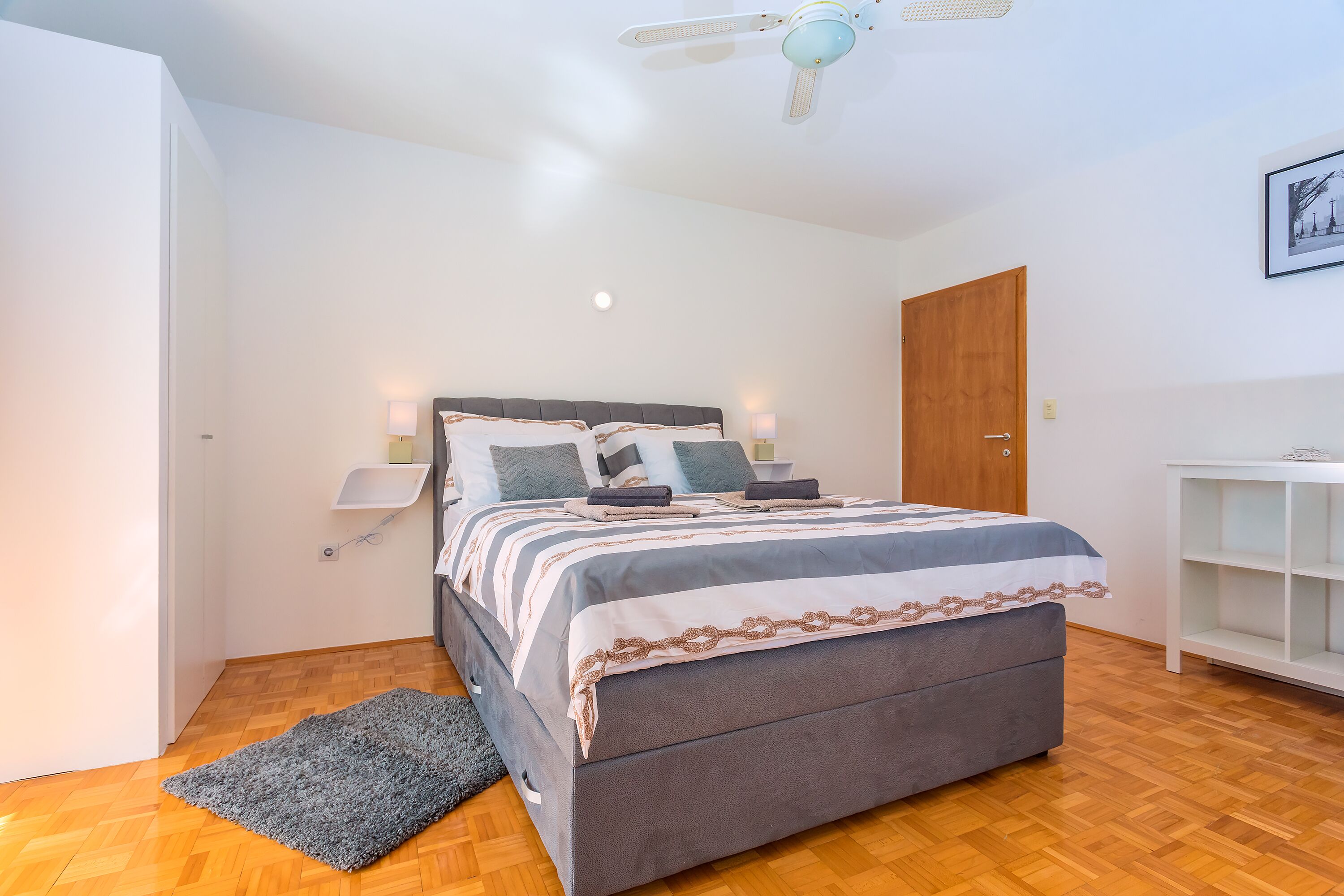 A bedroom with a bed, bedside tables, a ceiling fan, and a wooden wardrobe.