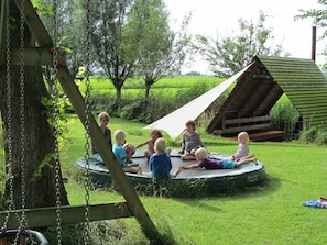 Children play on a grassy outdoor area with a wooden swing set and playhouse.