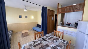 Ein kleiner Raum mit Bett, Esstisch, einer Küchenzeile und einem Deckenventilator.