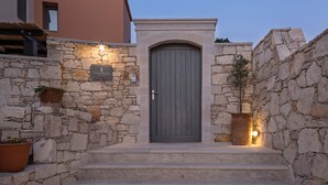 A stone-walled entrance with a grey door, steps leading up to it, and two lit wall sconces. -  Villa Levanda,pool, walking distance from the beach and shops ,no car needed! (Πάνορμος Rethymno, Crete)
