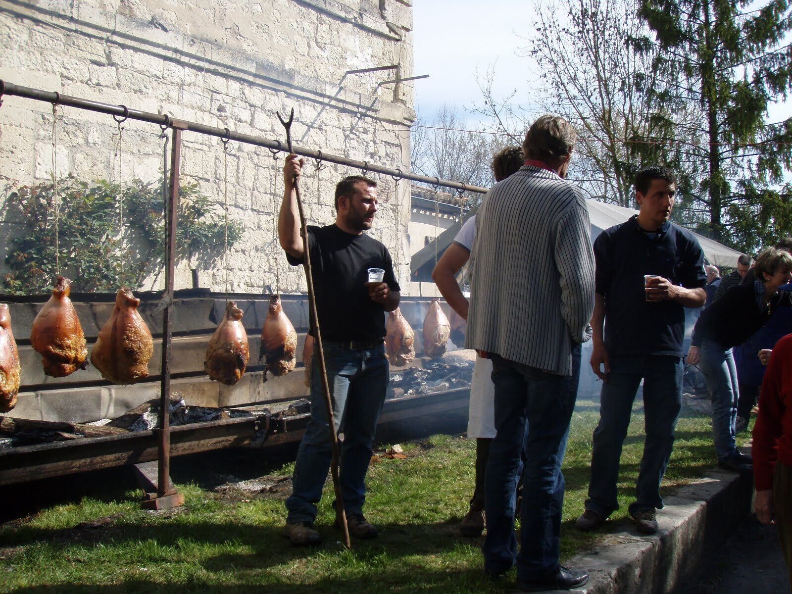 A group of people standing outdoors near a cooking area with hanging pots.