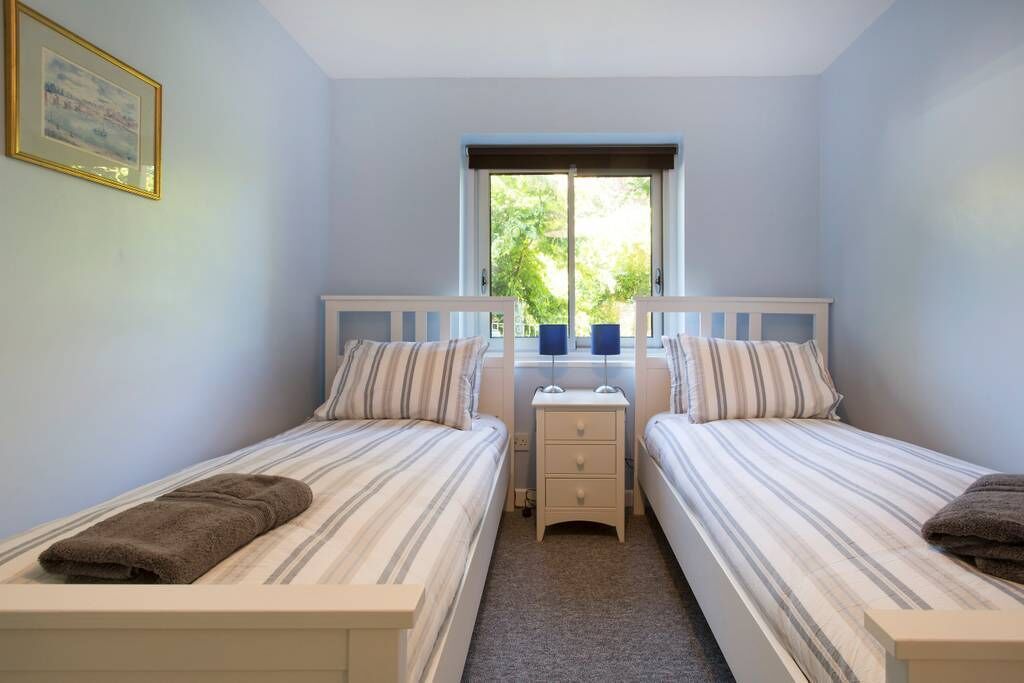 Une chambre avec deux lits simples, une petite table de chevet avec des lampes et une fenêtre donnant sur un paysage verdoyant.