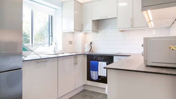 A modern kitchen with white cabinetry, a built-in dishwasher, and a window providing natural light. - Modern, Warm, Secure and Comfortable Oxford Apartment with easy access to City  (Oxford)