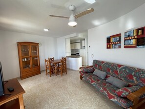 Una sala de estar con una mesa de comedor de madera, sillas, un sofá, un armario y un ventilador de techo.