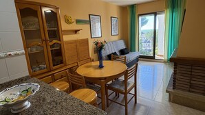 Un comedor con una mesa redonda y sillas, un aparador con puertas de vidrio, y un sofá al fondo.