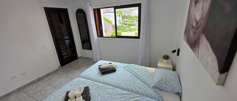 A hotel room with two beds, a window with a view of the street, and a small bedside table with a plant.