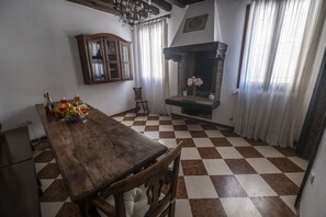 A dining area with a wooden table, chairs, a checkered floor, a fireplace, and a cabinet.