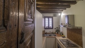 A kitchen with a wooden door, a window, a sink, a stove, and shelves with kitchen items. - VILLA FRARI IN CAMPIELLO (Venezia)