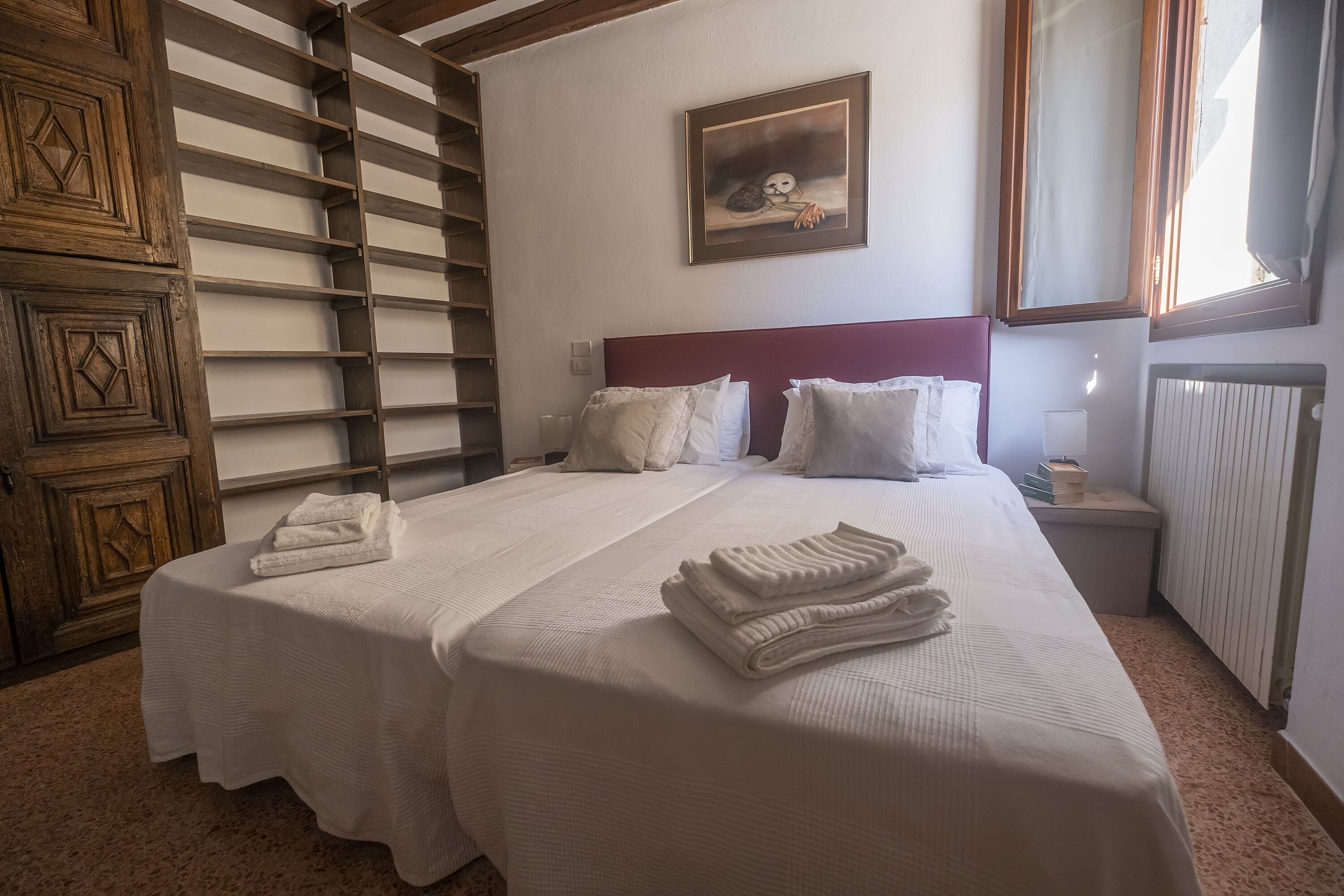 Un lit double avec du linge de lit blanc et des oreillers, une échelle en bois, un tableau accroché au mur et un radiateur.