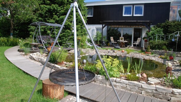 Une maison moderne dotée d’un patio, d’une balançoire et d’un petit étang.