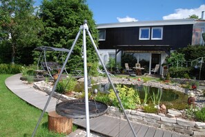 A modern house with a patio, a swing set, and a small pond. - Apartment Schneider (Mandelbachtal)