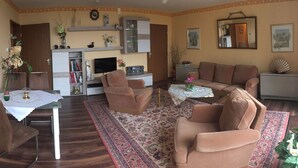 Un salon comprenant un canapé, des fauteuils, une table basse, un téléviseur et une bibliothèque.