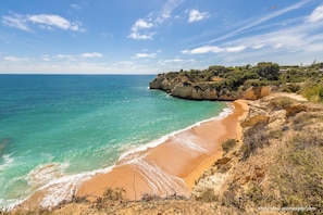A coastal landscape with a sandy beach, clear turquoise waters, and rocky cliffs.