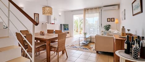 Un grand espace de vie comprenant une table à manger, des chaises en osier, un canapé et un téléviseur.