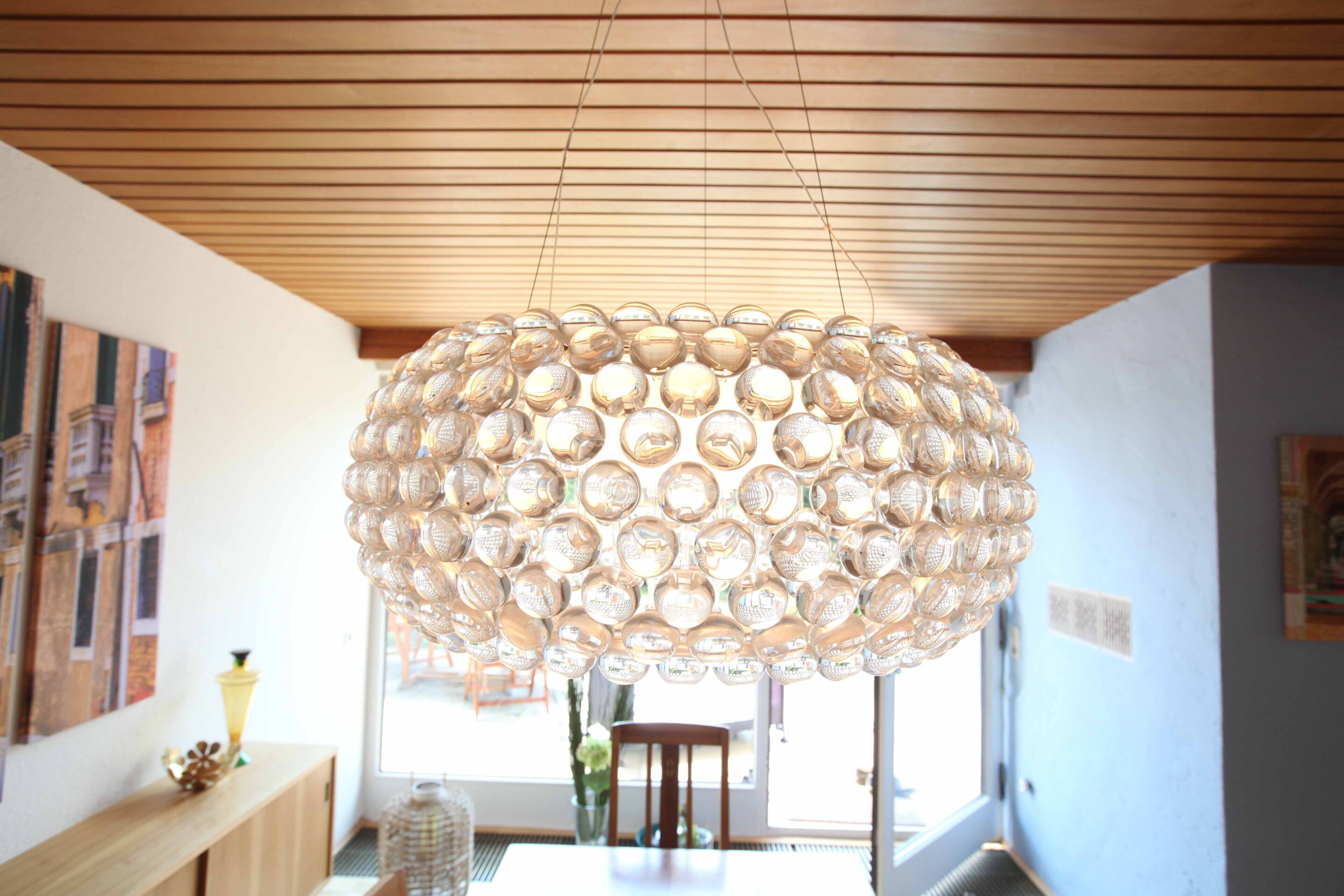 Ein Zimmer mit Holzbalkendecke, einer großen runden Chandelierleuchtre, einem Holztisch und einem Fenster mit Blick.