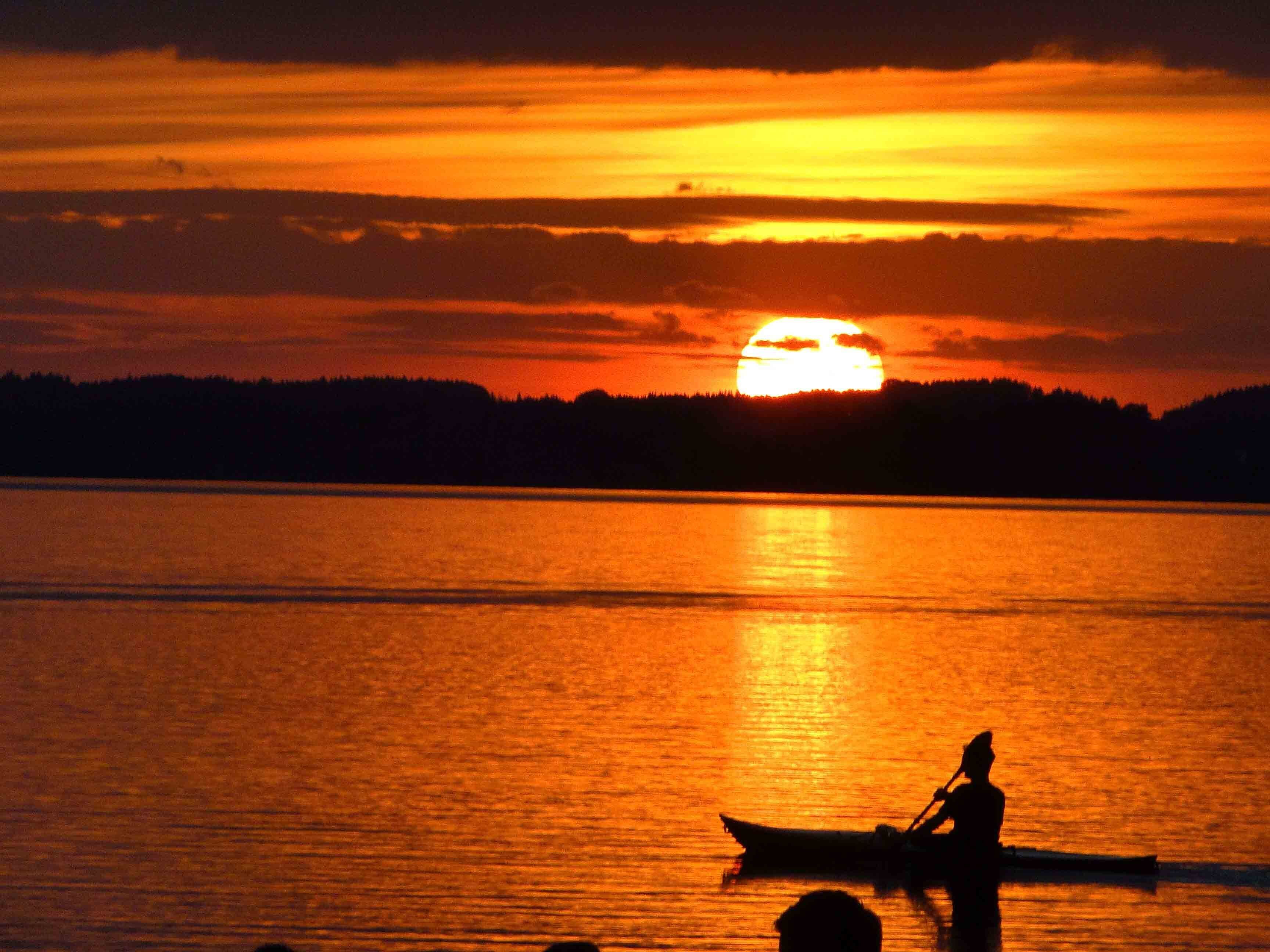 Solnedgang over en rolig sø med en silhuet af en person i en kano.