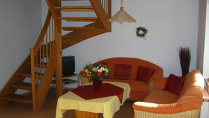 A living room with a wooden staircase, a sofa, a coffee table, and a TV. - Comfortable apartment with dream garden (Bleckede)