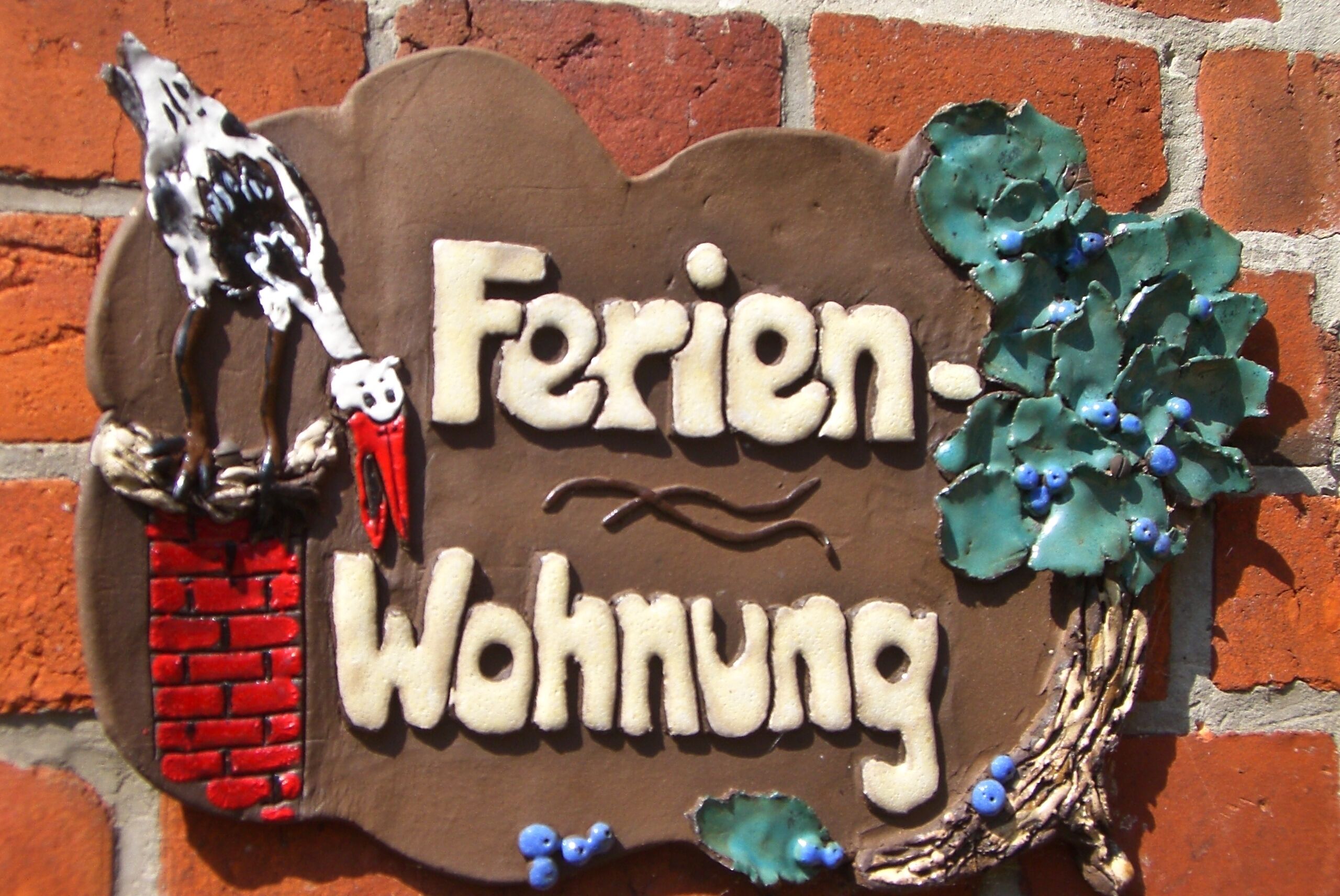 A sign with the text "Ferienwohnung" and decorative elements including a bird and holly leaves.