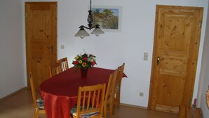 A dining area with a wooden table and chairs, a red tablecloth, a flower vase, and two wooden doors. - Comfortable apartment with dream garden (Bleckede)