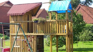 A wooden playhouse with a red roof, climbing wall, and a blue awning. - Comfortable apartment with dream garden (Bleckede)