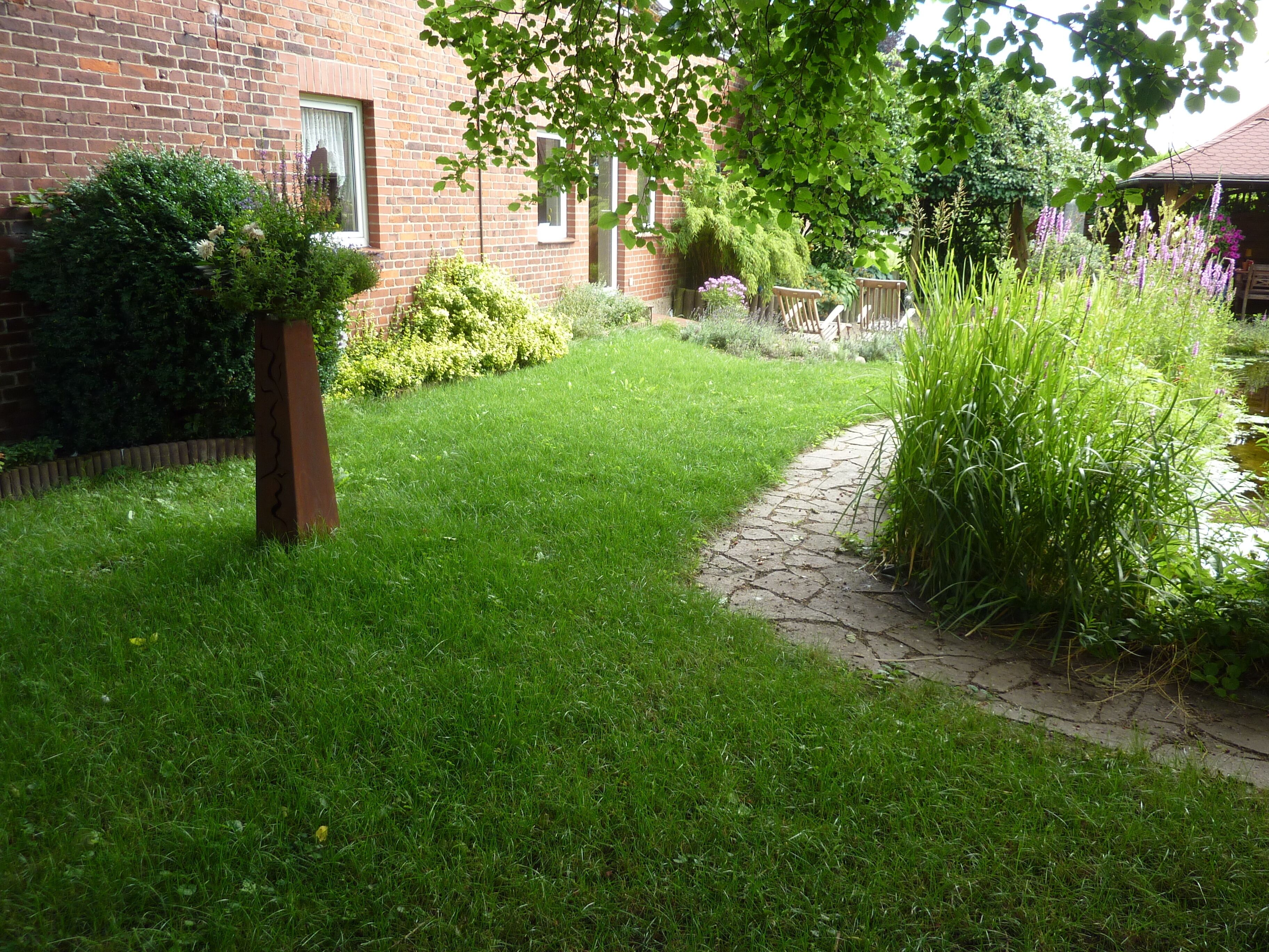 Un jardin bien entretenu, agrémenté d’un bâtiment en briques, d’un chemin en pierre et de diverses plantes.
