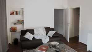 Ein Wohnzimmer mit einem dunkelbraunen Sofa, einem Glastisch und einem Bücherregal voller Bücher und Gesellschaftsspiele.