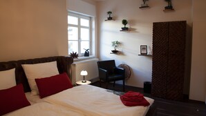 Ein Hotelzimmer mit einem großen Bett, einem Sessel, einem Heizkörper, einem Fenster und Wandregalen mit Pflanzen.