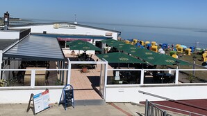 A rooftop terrace with outdoor seating, a view of the sea, and a sign for 'Strandcafé Randell'. - The family-friendly Villa Linus is located in a vacation park behind the dyke (Butjadingen)