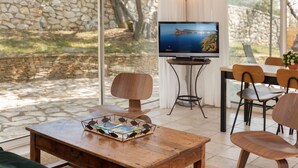 Una sala de estar moderna con una pared de piedra, un televisor, muebles de madera y vistas a un paisaje costero.