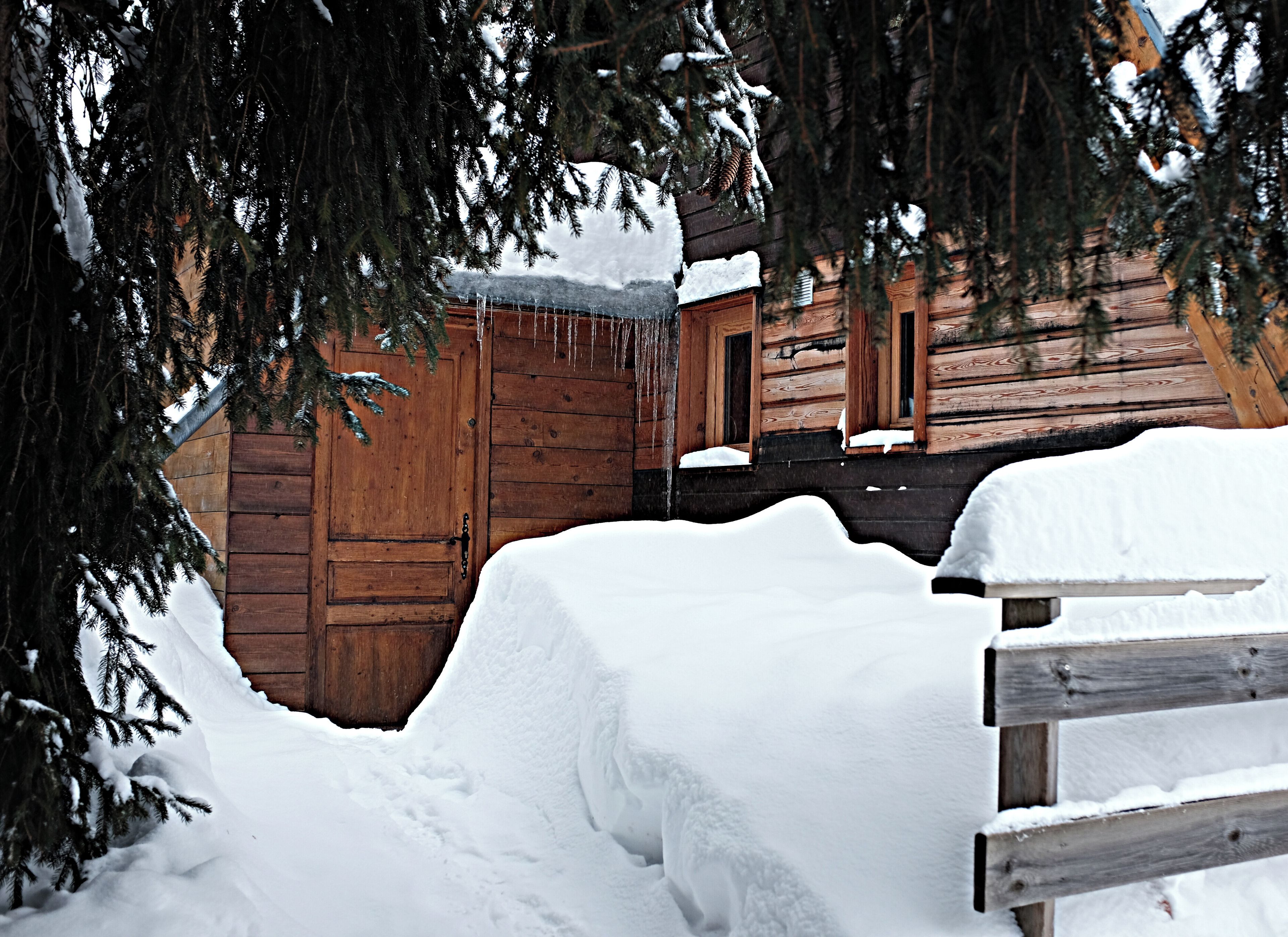 A wooden cabin with a snow-covered entrance and a wooden bench in front.
