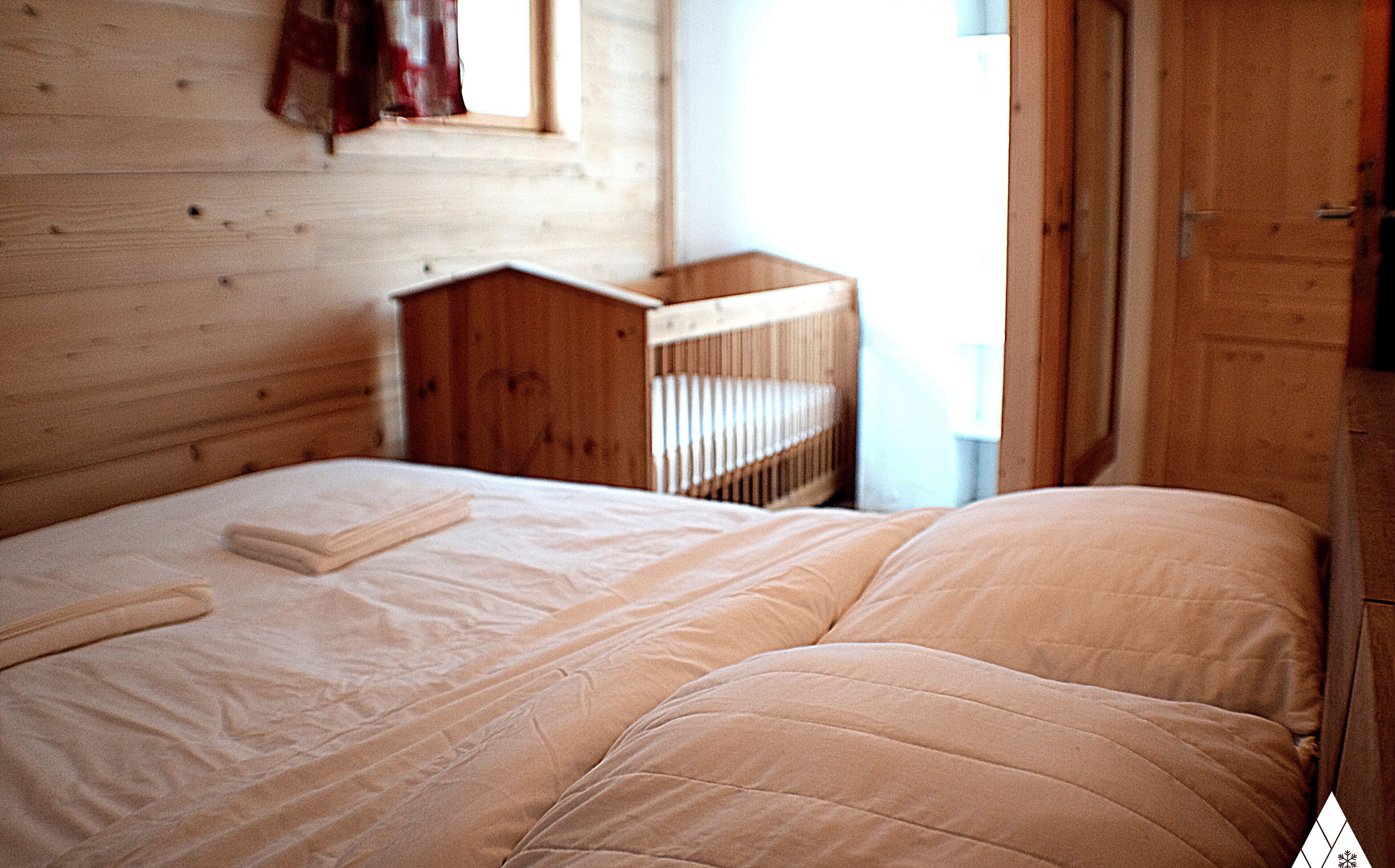 Een kamer met houten vloeren, een bed, een ledikant en een kledingkast.