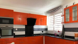 Une cuisine avec des meubles de couleur rouge, une cuisinière noire et une fenêtre avec des stores.