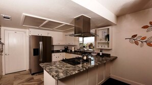 Une cuisine moderne dotée d’un îlot central, d’appareils électroménagers en acier inoxydable et d’une décoration murale représentant des motifs de feuilles.