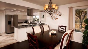 Une cuisine moderne avec des meubles blancs, un îlot central et un coin repas comprenant une table et des chaises en bois foncé.